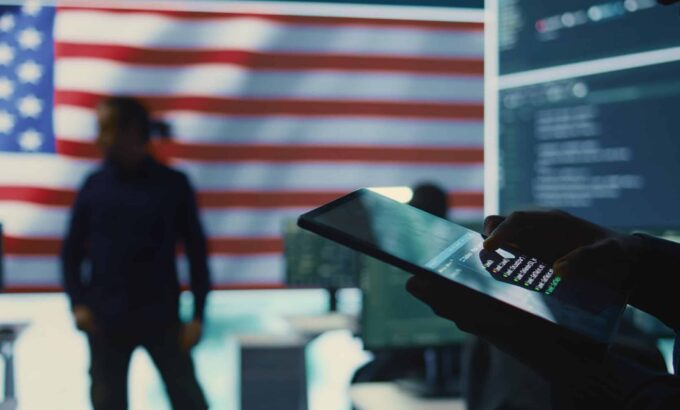 Cybersecurity expert in a governmental IT environment with the American flag. Monitoring cybersecurity, encryption and data security on a tablet to protect against cyber threats. Close up. Camera B.